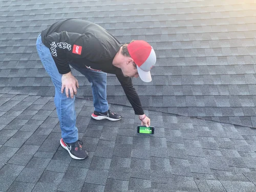 Roofing professional inspecting and photographing a shingle roof to document damage for an insurance claim